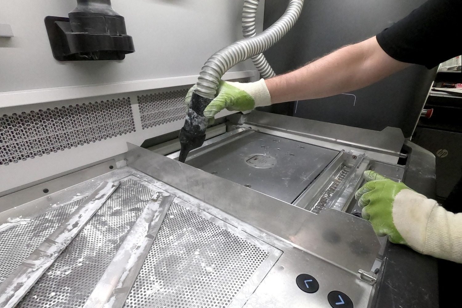 Gloved hands using cleaning equipment on stainless-steel kitchen components.