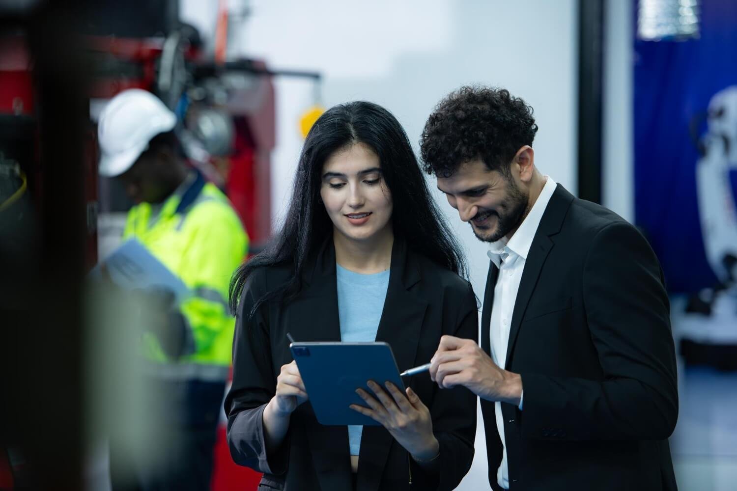 Two professionals reviewing a tablet inside a working facility.