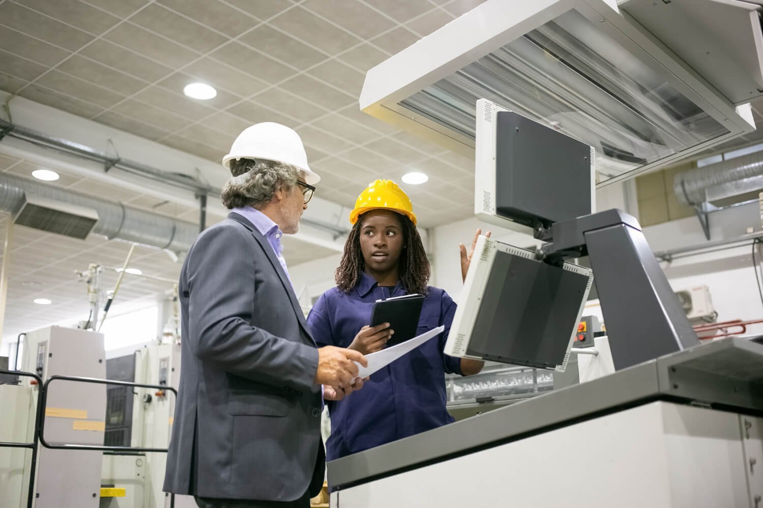Two professionals reviewing equipment beside machinery in a commercial facility.