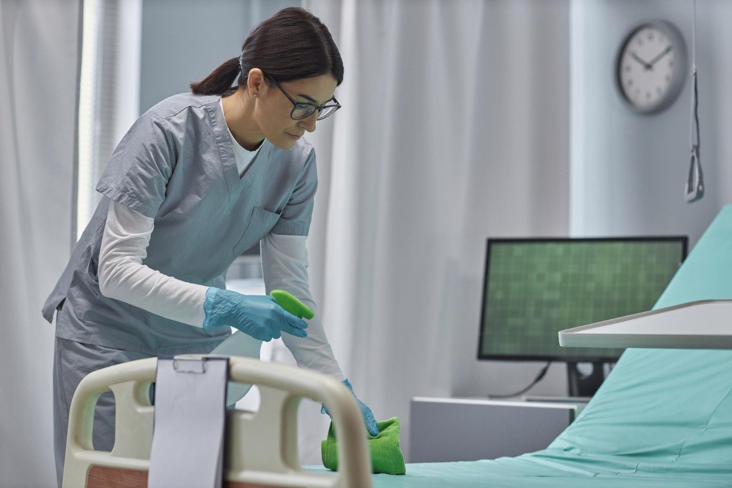 A cleaner wiping the bed area in a healthcare room.