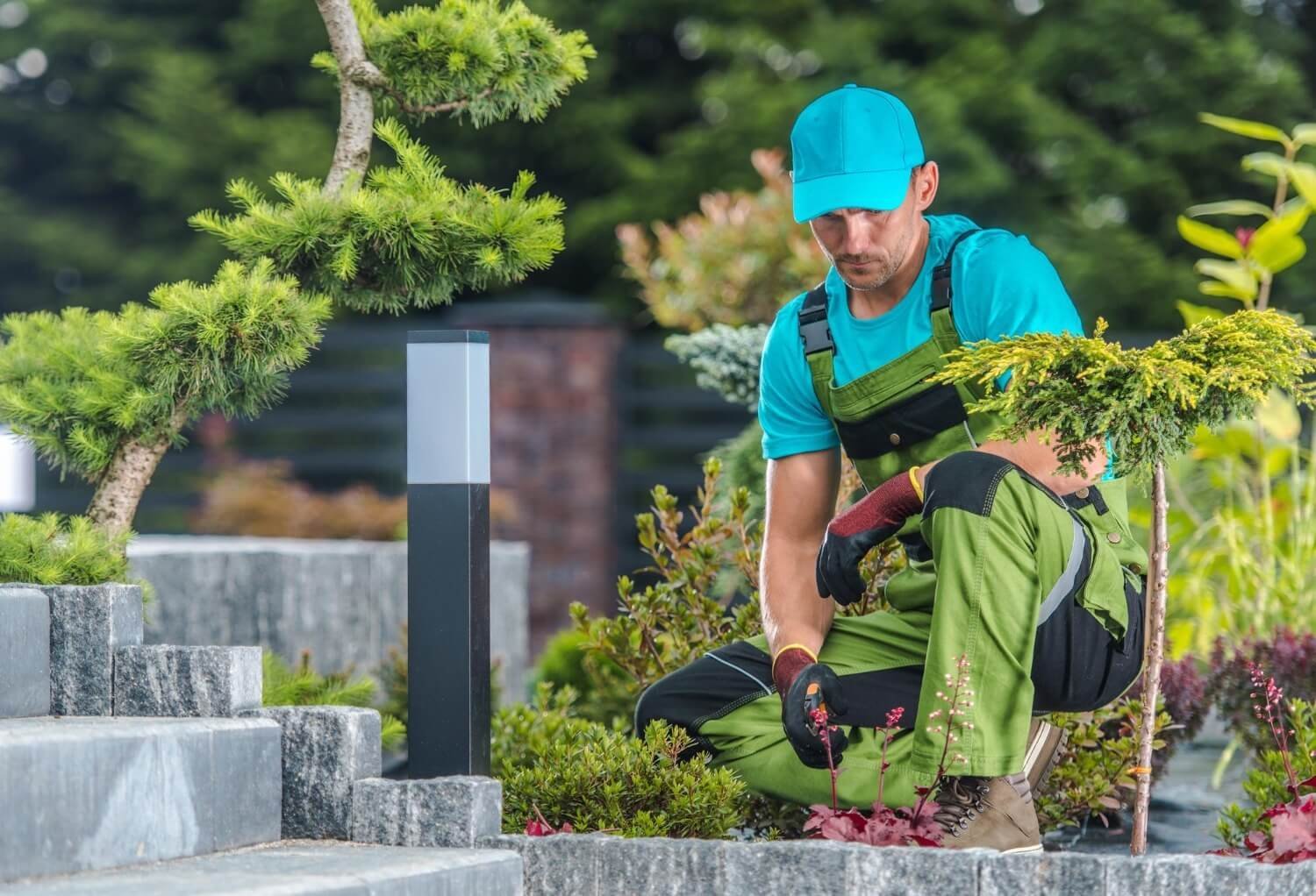 A grounds professional tending planting beds beside a landscaped walkway.