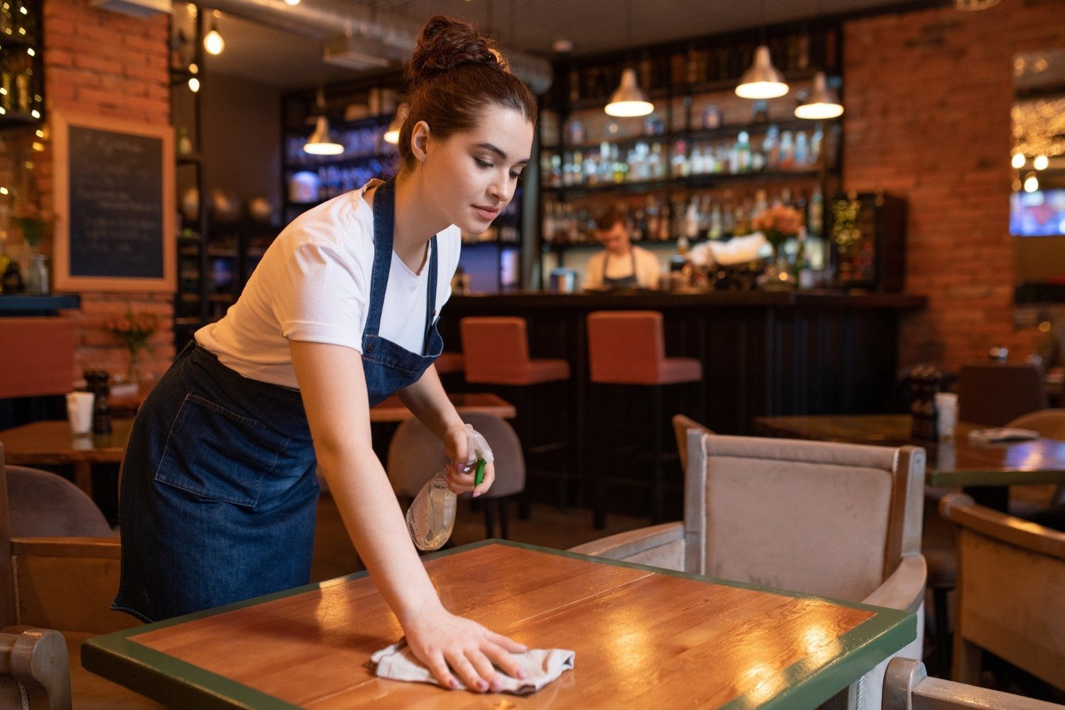 A staff member wiping a table in a restaurant dining area.